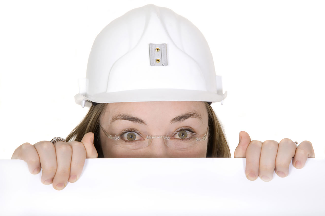 woman in white hard hat peeking behind wall 